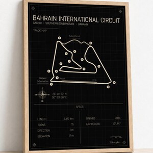 May include: A framed print featuring a technical blueprint of the Bahrain International Circuit in Sakhir. The black background displays a white track map, numbered turns, compass, and specifications including a 5.412 km length and 2004 opening date.