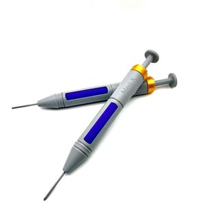 May include: Two gray syringe-like tools with blue rectangular inlays and gold-colored collars. Each device features a thin metal needle at the tip and a plunger mechanism at the end. The text Med-X is printed in black on the barrel of one device.