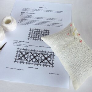 May include: A white embroidery project with instructions for a four-sided stitch. The project is on a white pillow with pink pins. The instructions include a diagram of the stitch and the text "Band 2 - Four-sided stitch".