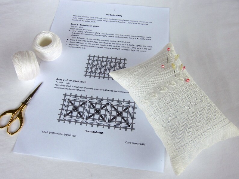 May include: A white embroidery project with instructions for a four-sided stitch. The project is on a white pillow with pink pins. The instructions include a diagram of the stitch and the text "Band 2 - Four-sided stitch".