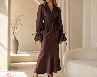 May include: A dark brown two-piece set consisting of a long-sleeved wrap top with a tie waist and flared cuffs, paired with a matching floor-length satin skirt. The top features a V-neckline and sheer fabric, while the skirt has a smooth finish.