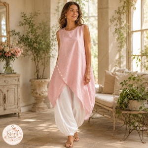 May include: A sleeveless light pink tunic top featuring an asymmetrical hemline with a diagonal row of white buttons, paired with loose-fitting white trousers. The ensemble is presented with a soft, light-coloured aesthetic and clean lines.