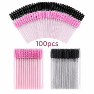 Op de afbeelding: Een verzameling van 100 wegwerp wimperborstels gerangschikt in een waaier, met extra sets roze en zwarte borstels in doorzichtige rechthoekige verpakkingen. De borstels hebben roze handvatten en ofwel zwarte of roze borstelkoppen.