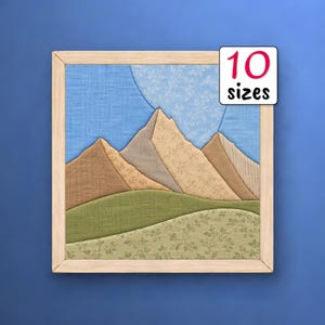 May include: A square fabric wall art piece in a light wood frame featuring a mountain landscape. The scene includes layered fabric sections in shades of brown, tan, and green with floral patterns, set against a blue sky. Text reads 10 sizes.