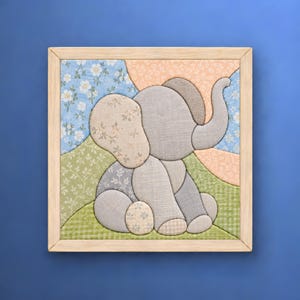 May include: A square framed fabric wall art piece featuring a patchwork elephant in shades of gray and beige. The elephant is set against a background of blue floral, green vine, and peach patterned fabric patches within a light wood frame.