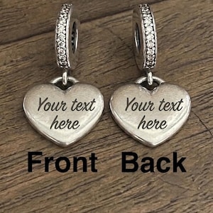 K&ouml;nnte beinhalten: Zwei silberfarbene herzf&ouml;rmige Anh&auml;nger mit einer &Ouml;se, die mit klaren Steinen besetzt ist. Jeder Anh&auml;nger ist mit dem Text 'Your text here' graviert. Das Bild enth&auml;lt die Beschriftungen 'Front' und 'Back' zur Kennzeichnung der Ausrichtung.