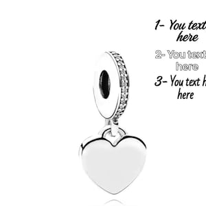 K&ouml;nnte beinhalten: Ein silberfarbener herzf&ouml;rmiger Anh&auml;nger mit einer runden &Ouml;se, die mit einer Reihe klarer Steine besetzt ist. Rechts steht der Text: 1- You text here, 2- You text here, 3- You text here. Der Anh&auml;nger hat eine glatte, polierte Oberfl&auml;che.