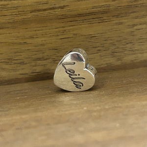 K&ouml;nnte beinhalten: Ein herzf&ouml;rmiger Charm-Anh&auml;nger aus Silber mit polierter metallischer Oberfl&auml;che. Der Name Leila ist in Schreibschrift auf die Vorderseite des Herzens graviert. Der Anh&auml;nger verf&uuml;gt &uuml;ber eine mittige &Ouml;ffnung zum Auff&auml;deln auf Ketten.