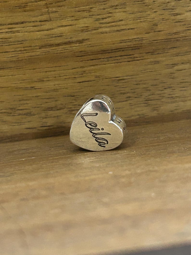 K&ouml;nnte beinhalten: Ein herzf&ouml;rmiger Charm-Anh&auml;nger aus Silber mit polierter metallischer Oberfl&auml;che. Der Name Leila ist in Schreibschrift auf die Vorderseite des Herzens graviert. Der Anh&auml;nger verf&uuml;gt &uuml;ber eine mittige &Ouml;ffnung zum Auff&auml;deln auf Ketten.