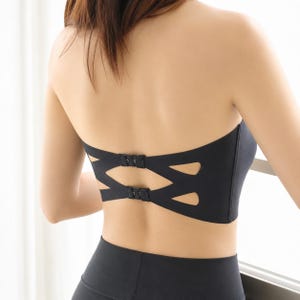 May include: Black strapless bra with a unique cut-out design on the back. The bra features two sets of hook-and-eye closures and is paired with black athletic wear. The bra's design includes geometric cutouts.