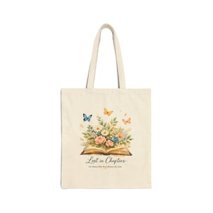 Peut inclure: Sac fourre-tout crème avec une illustration à l'aquarelle d'un livre ouvert, de fleurs et de papillons. Le texte "Lost in Chapters" et "For Women Who Read Between the Lines" est imprimé en dessous.