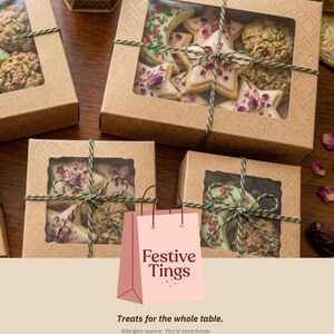 May include: Several boxes of cookies with clear window tops, tied with green twine. The cookies are star-shaped and round, decorated with icing and sprinkles. A pink shopping bag with the text "Festive Tings" is in the foreground.