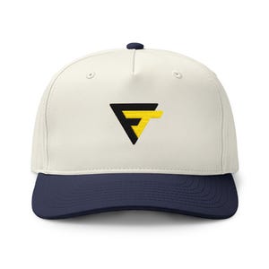 May include: A five-panel baseball cap featuring an off-white crown and a dark navy blue brim. The front center displays an embroidered logo consisting of a black triangle shape combined with a bright yellow letter T, forming a stylized FT design.