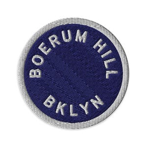May include: Circular embroidered patch featuring the text "BOERUM HILL BKLYN" in white against a navy blue background. The patch has a silver-grey border and a textured finish.