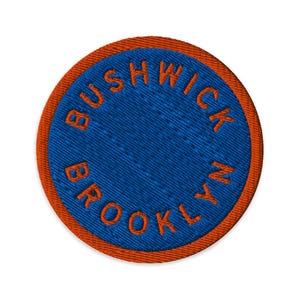 May include: Embroidered patch with the words "Bushwick Brooklyn" in orange thread on a blue background. The patch has an orange border and is circular in shape. The text is in a bold, sans-serif font.