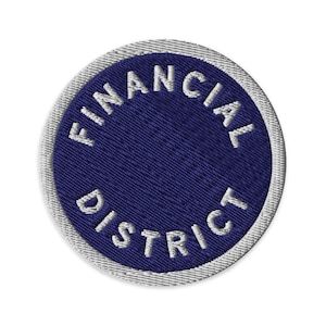 Könnte beinhalten: Ein kreisförmiger gestickter Aufnäher mit einer tiefblauen Mitte und dem weißen Text FINANCIAL DISTRICT, der in einem geschwungenen Muster entlang des Randes gestickt ist, abgeschlossen mit einem dicken weißen Rand.