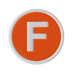 May include: Embroidered patch featuring a white letter "F" on a bright orange background. The letter is centered within a circular design, bordered by a white stitched edge. The patch has a textured appearance, suggesting it is made of fabric.