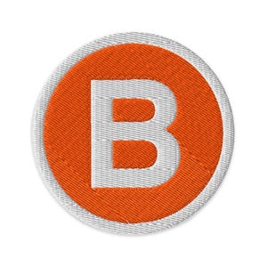 May include: Circular embroidered patch with a white letter "B" in a vibrant orange circle. The orange circle is framed by a white stitched border. The patch has a textured finish and is circular in shape.