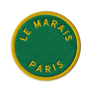 Peut inclure: Un écusson brodé circulaire avec un centre vert profond et une bordure épaisse jaune doré. Le texte LE MARAIS est brodé en fil jaune doré le long de la courbe supérieure, et le mot PARIS est brodé dans la même couleur en dessous.