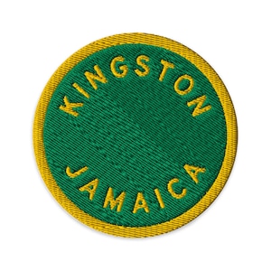May include: A circular embroidered patch featuring a solid green center surrounded by a yellow border. The text KINGSTON is embroidered in yellow along the top curve, and the text JAMAICA is embroidered in yellow along the bottom curve.