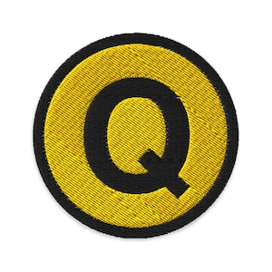 May include: Embroidered patch featuring the letter "Q" in black, centered within a yellow circle. The circle is outlined with a black border. The patch has a textured, stitched appearance, suitable for apparel or accessories.