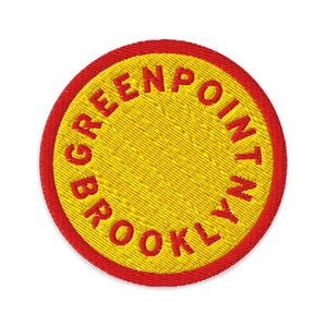 May include: Embroidered patch with a yellow center and a red border. The text "GREENPOINT BROOKLYN" is embroidered in red around the yellow center. The patch is circular and has a textured appearance.