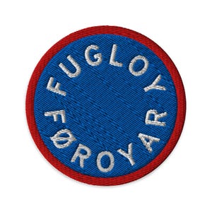 Op de afbeelding: Geborduurde patch met een blauw midden en een rode rand. De patch heeft de witte tekst "FUGLOYAR", gebogen rond het blauwe midden. Het ontwerp is cirkelvormig en heeft een getextureerd uiterlijk.