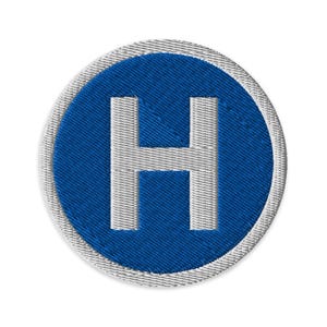 May include: Embroidered patch featuring a white letter "H" on a blue circular background. The patch has a white border and a textured appearance. The design is simple and bold, suitable for various applications.