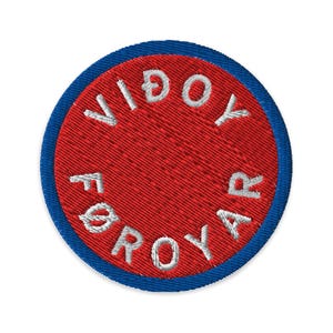 Könnte beinhalten: Runder, gestickter Aufnäher mit roter Mitte und blauem Rand. Der weiße Text "VIDOY FØROYAR" ist um den roten Kreis gestickt. Der Aufnäher hat ein strukturiertes Aussehen.