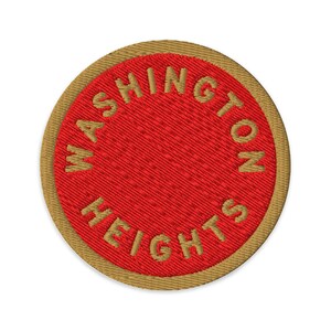 May include: A circular embroidered patch featuring a vibrant red center surrounded by a tan border. The text WASHINGTON HEIGHTS is stitched in tan thread, following the circular curve of the patch along the inner edge of the border.