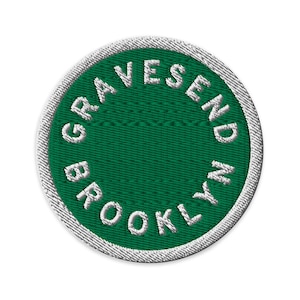 Peut inclure: Un écusson brodé circulaire avec un fond vert foncé et une bordure blanche. Le texte GRAVESEND BROOKLYN est brodé en lettres capitales blanches suivant un motif circulaire le long du bord intérieur, laissant le centre vide.