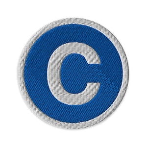 Puede incluir: Parche bordado con el símbolo de copyright azul, un borde blanco y un fondo blanco. El símbolo azul es una letra "C" estilizada dentro de un círculo, con una apariencia texturizada.