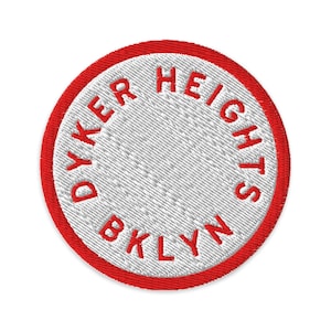 Op de afbeelding: Een ronde geborduurde patch met een wit midden en een dikke rode rand. De tekst DYKER HEIGHTS BKLYN is in rode hoofdletters langs de binnenrand geborduurd, wat een cirkelvormig patroon vormt op de witte achtergrond.