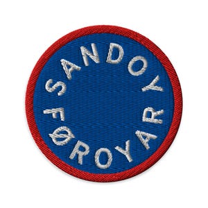 May include: Circular embroidered patch with a blue centre and a red border. The patch features white text in a circular arrangement that reads "SANDOYAR FØROYAR". The patch is round and has a textured appearance.