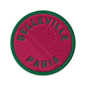 Puede incluir: Un parche bordado circular con un centro magenta vibrante y un borde verde oscuro. El texto BELLEVILLE PARIS está bordado en letras mayúsculas de color verde oscuro, curvándose a lo largo de los bordes superior e inferior del campo.