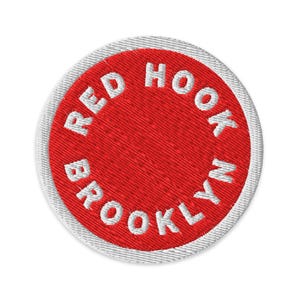 May include: Embroidered patch with a red center and white text that reads "RED HOOK BROOKLYN". The patch has a white border and is circular in shape. The text is in a bold, sans-serif font.