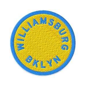 May include: Embroidered patch with a yellow center and a blue border. The text "WILLIAMSBURG BKLYN" is embroidered in blue around the yellow center. The patch is circular.