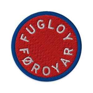 Op de afbeelding: Geborduurde ronde patch met een rode kern en een blauwe rand. De witte tekst "FUGLOYAR" is rond de kern geborduurd. De patch heeft een getextureerd uiterlijk.