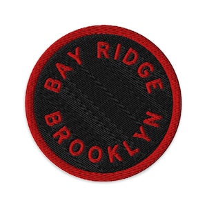 May include: A circular embroidered patch featuring a black background with a red border. The text BAY RIDGE BROOKLYN is stitched in red capital letters following the curve of the circle. The patch has a visible fabric texture throughout.