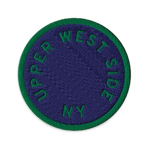 May include: A circular embroidered patch featuring a deep purple center and a vibrant green border. The text "UPPER WEST SIDE NY" is stitched in green thread, following the circular curve of the patch along the inner edge of the border.