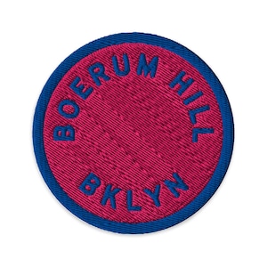 Puede incluir: Un parche bordado circular con un centro magenta vibrante y un borde azul oscuro. El texto BOERUM HILL está bordado con hilo azul oscuro a lo largo de la curva superior, y la abreviatura BKLYN está bordada en azul oscuro en la parte inferior.
