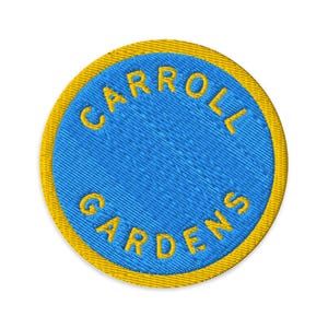 Op de afbeelding: Ronde geborduurde patch met de tekst "CARROLL GARDENS" in geel op een blauwe achtergrond, met een gele rand. De patch heeft een getextureerde afwerking, ontworpen voor toepassing op kleding of accessoires.
