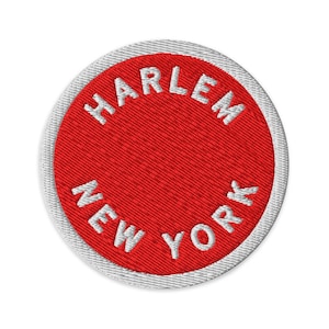Pode incluir: Um emblema bordado circular com um fundo vermelho vibrante e uma borda branca. O texto HARLEM está arqueado no topo e NEW YORK na parte inferior em letras bordadas brancas, em maiúsculas e sem serifa.