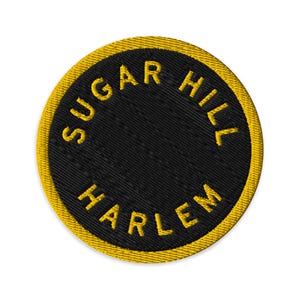 Puede incluir: Un parche bordado circular con fondo negro y un borde amarillo grueso. El texto SUGAR HILL está arqueado en la parte superior y la palabra HARLEM está arqueada en la parte inferior, ambos bordados en letras mayúsculas amarillas y negritas.