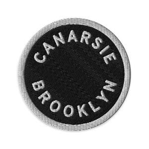 May include: A circular embroidered patch featuring a black background with a white border. The text CANARSIE BROOKLYN is stitched in white capital letters following the curve of the circle along the top and bottom edges of the patch.