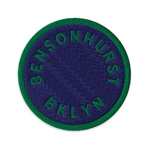 Peut inclure: Un écusson brodé circulaire avec un centre violet foncé et une bordure vert vif. Le texte BENSONHURST BKLYN est cousu en fil vert selon un motif circulaire le long du bord intérieur de l'écusson, créant un contraste marqué.