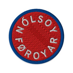 May include: Embroidered patch with a red center and a blue border. The red center features white text in a circular pattern. The text reads "FØLSOYAR ROYAR". This patch is likely for clothing or accessories.