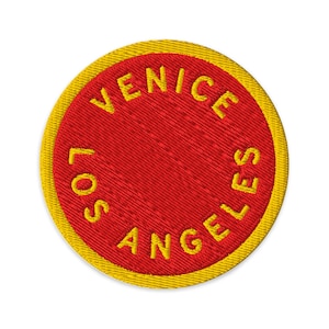 Könnte beinhalten: Ein kreisförmiger gestickter Aufnäher mit einer leuchtend roten Mitte und einem dicken gelben Rand. Der Text VENICE LOS ANGELES ist in gelben Großbuchstaben gestickt und verläuft entlang des inneren Randes des roten kreisförmigen Feldes.
