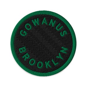 Op de afbeelding: Geborduurde ronde patch met de tekst "GOWANUS BROOKLYN" in groene letters op een zwarte achtergrond. De patch heeft een groene rand. Ontworpen om op kleding of accessoires te naaien.