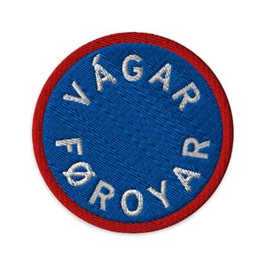May include: Circular embroidered patch featuring the text "VÁGAR FØROYAR" in white on a blue background, with a red border. Suitable for application on clothing or accessories.